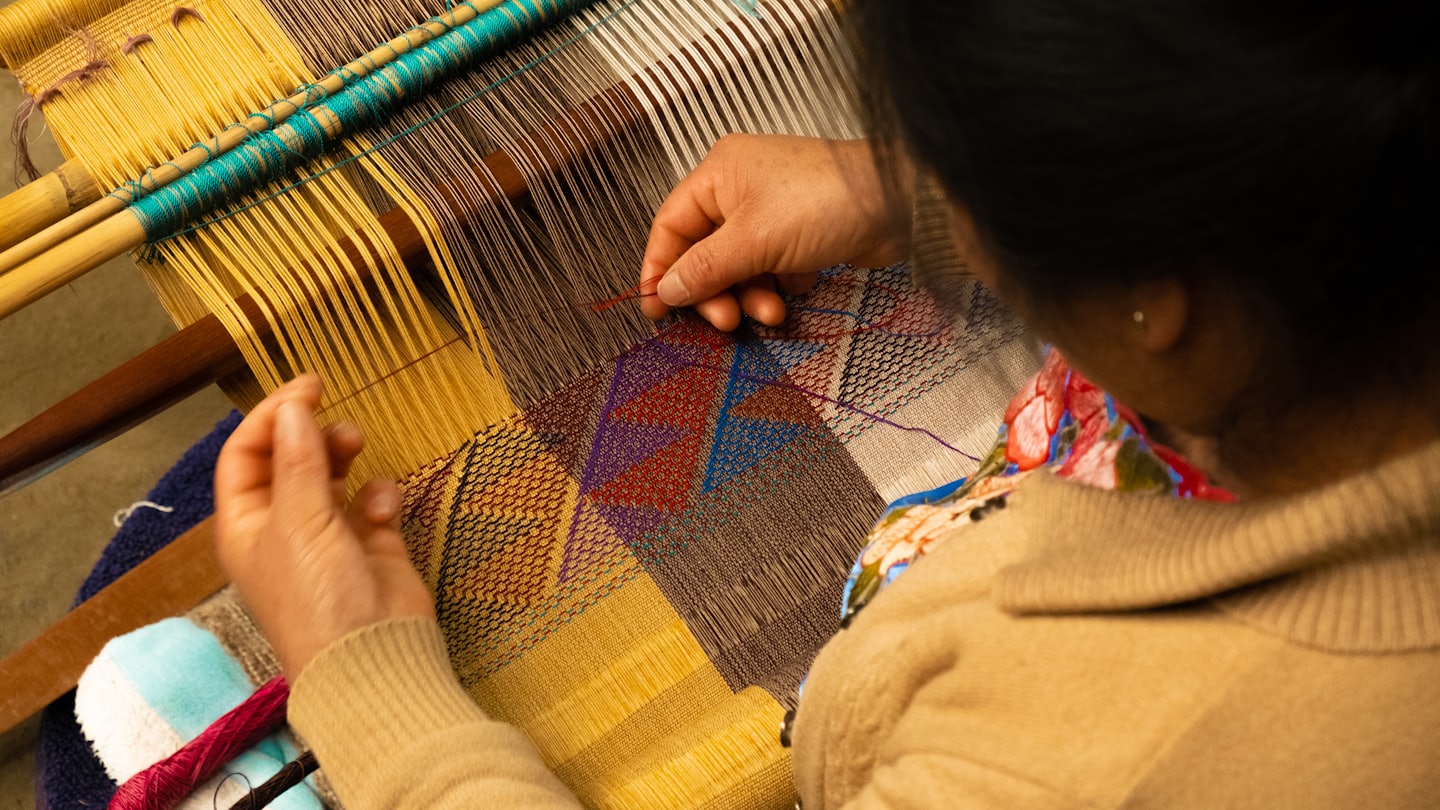 A woman threading embroidery on a loom.