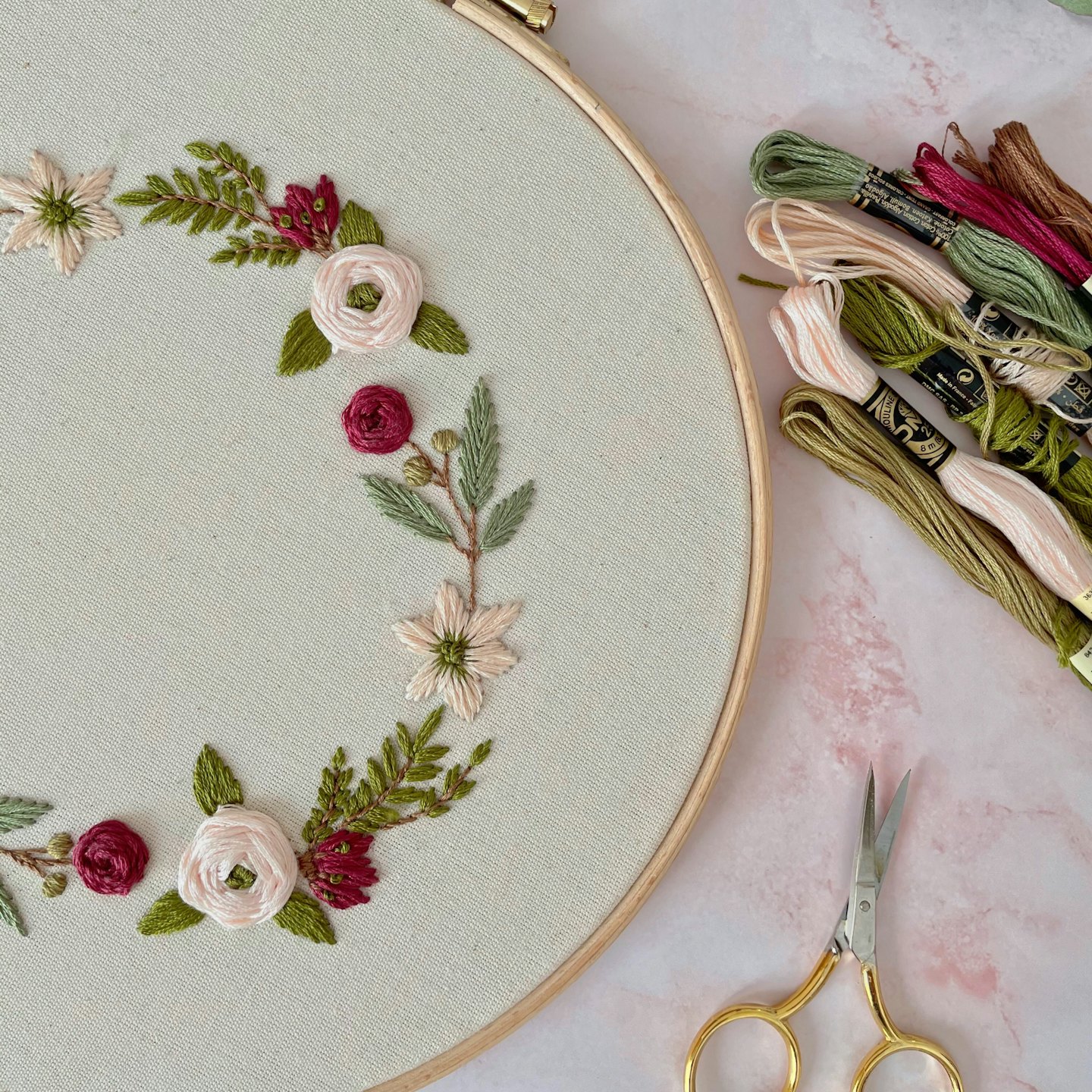 Embroidery hoop with floral embroidery, next to a pair of golden scissors and a bunch of twines.