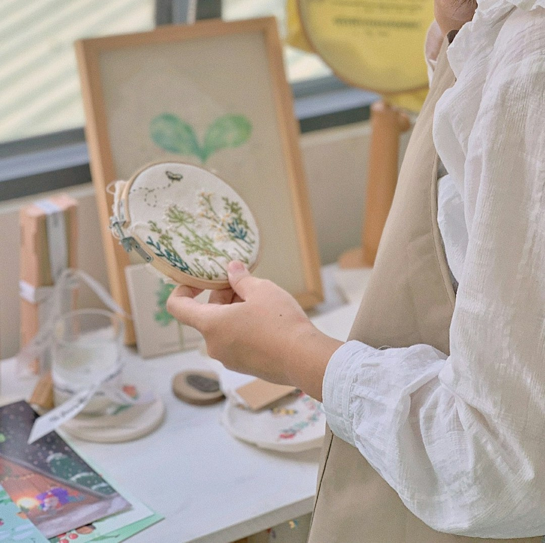 Hand holding an embroidery hoop with floral patterns and a bee.